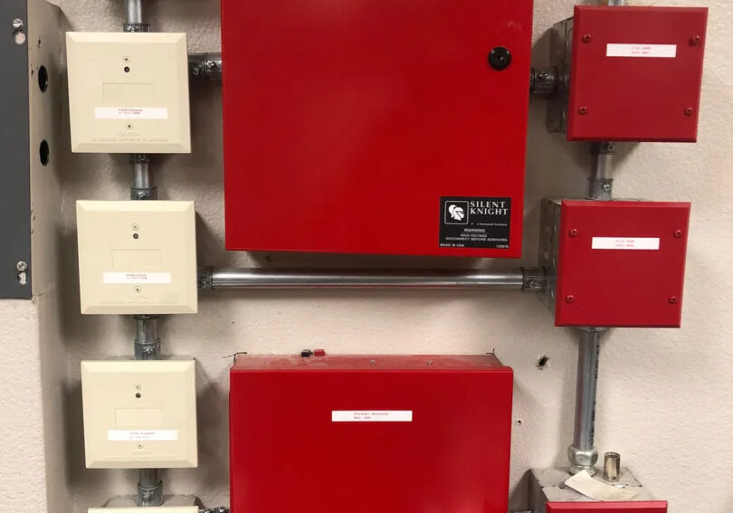 A red fire alarm system with many boxes attached to it.